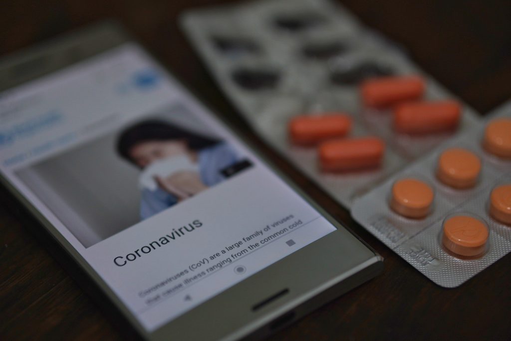 Tablettenpackungen und ein angeschaltetes Smartphone auf dem ein Beitrag über den Coronavirus zu sehen ist