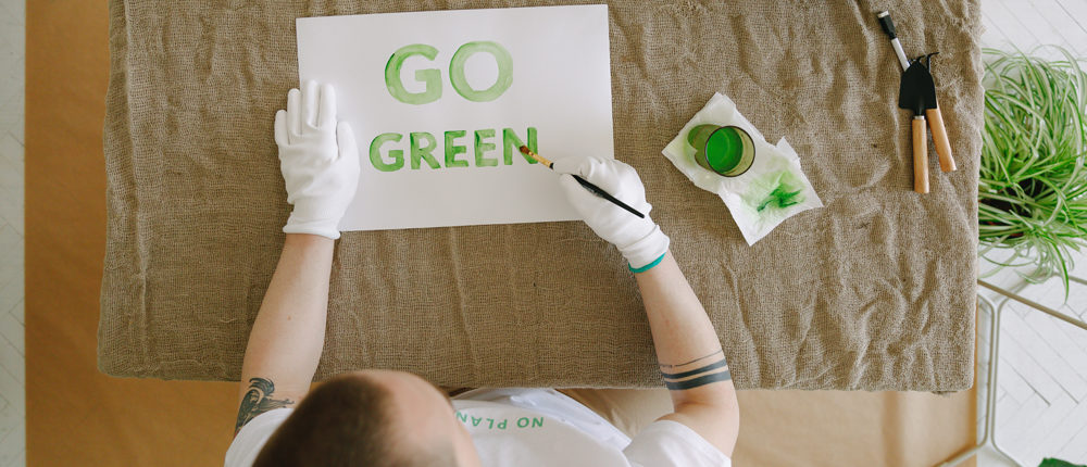 Mann malt den Text "Go Green" mit grüner Farbe auf