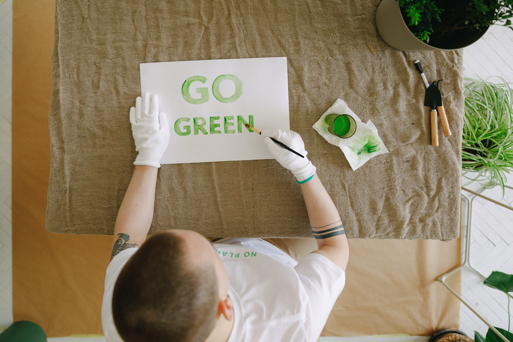 Mann malt den Text "Go Green" mit grüner Farbe auf